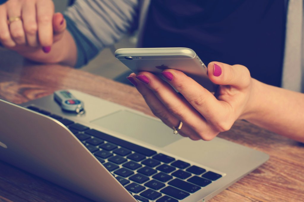 A hand holding a phone over a laptop